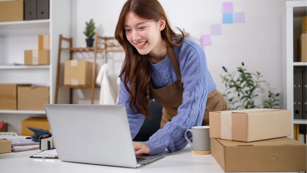 Young entrepreneur smiling while working on a laptop with packages around her desk