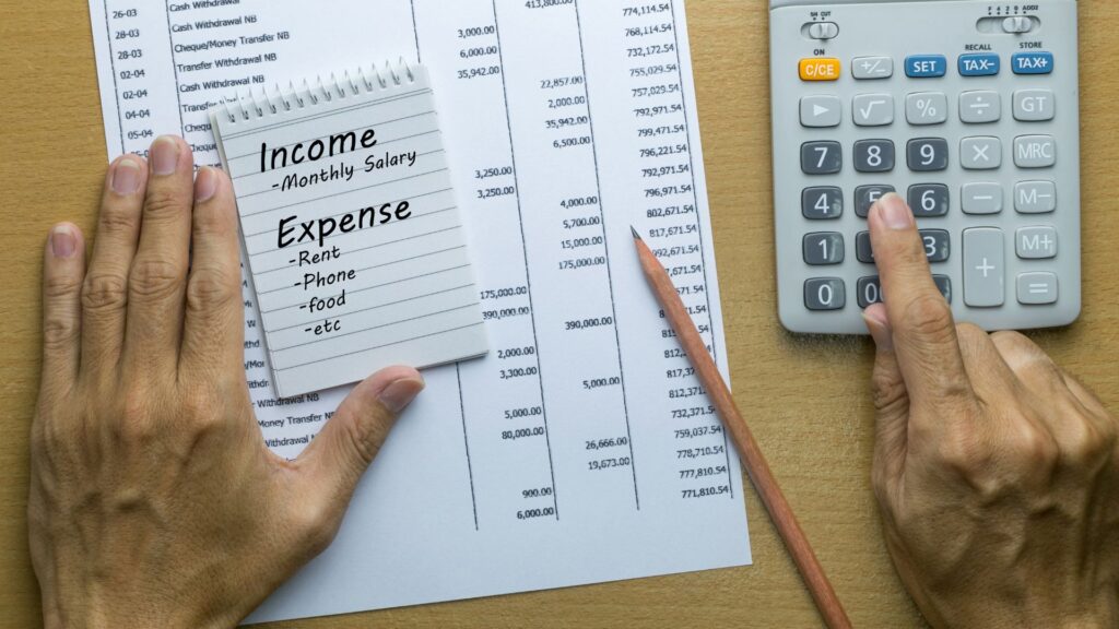 Person using a calculator with a notepad showing income and expenses written down